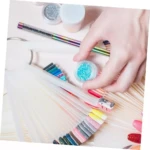 Mano sosteniendo tarro con escarcha azul sobre abanico de muestras para uñas, junto a un pincel delineador Kolinsky con cuerpo iridiscente.