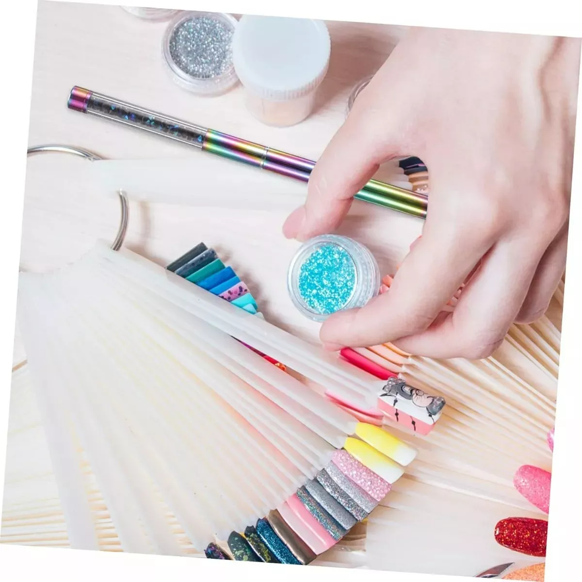 Mano sosteniendo tarro con escarcha azul sobre abanico de muestras para uñas, junto a un pincel delineador Kolinsky con cuerpo iridiscente.