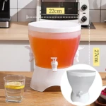 Dispensador de bebidas transparente de 3 compartimentos con grifo y vaso de limonada al lado.