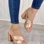 Sandalias de tacón cuadrado color oro rosa con diseño de tiras cruzadas en el empeine, puestas en un pie con tobillera dorada y jean azul. Referencia GS 205.