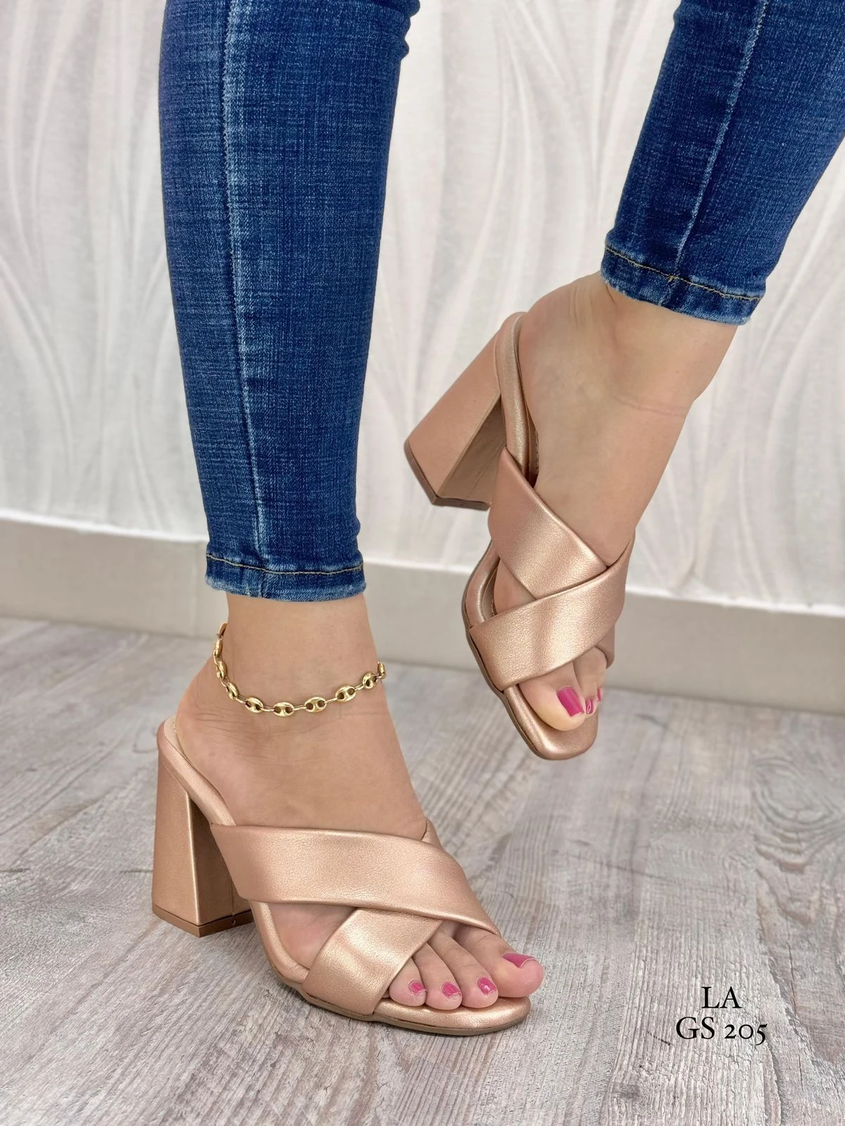 Sandalias de tacón cuadrado color oro rosa con diseño de tiras cruzadas en el empeine, puestas en un pie con tobillera dorada y jean azul. Referencia GS 205.
