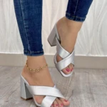 Sandalias de tacón cuadrado color plata con tiras cruzadas en el empeine, usadas con jeans y tobillera dorada sobre piso de madera. Modelo LA GS 205.