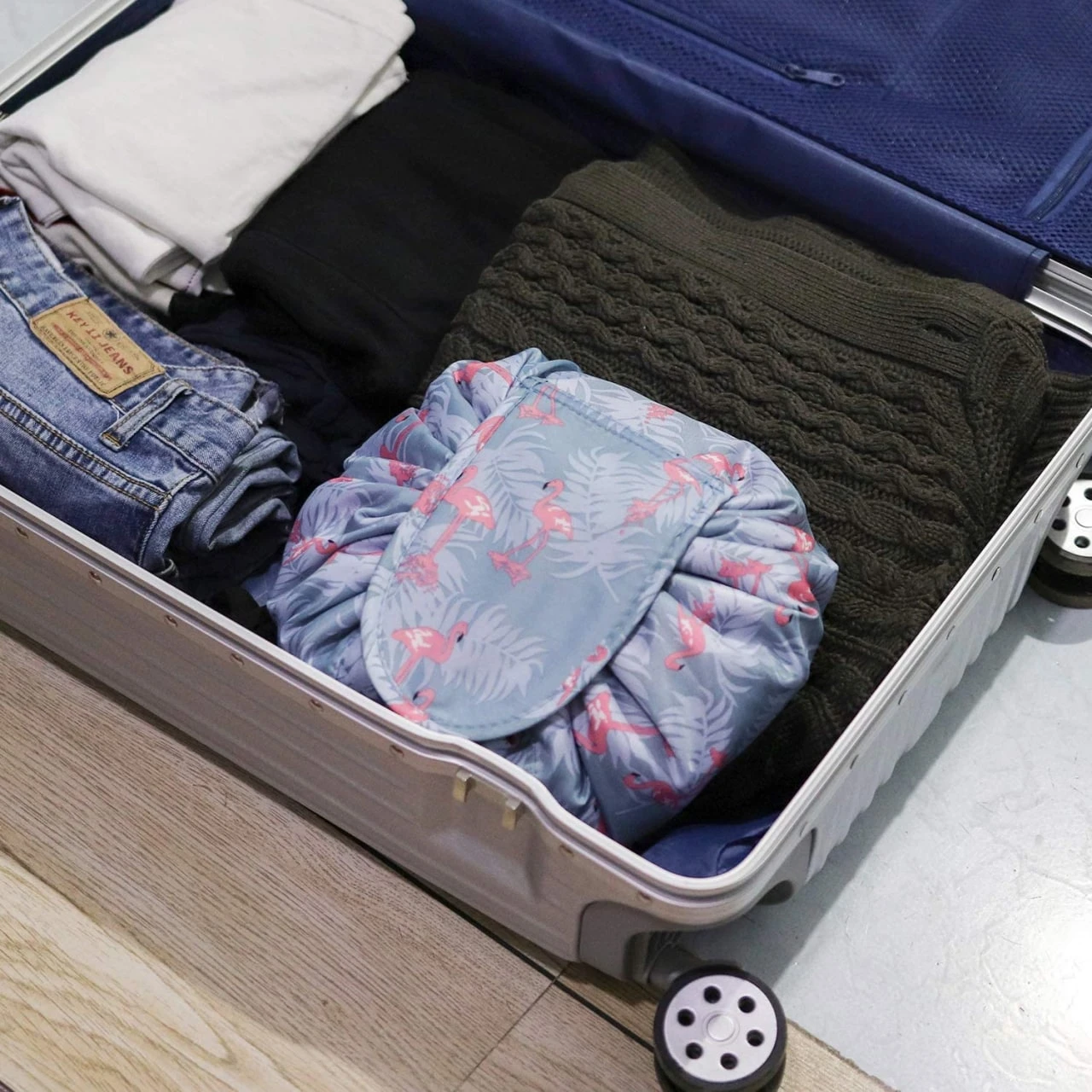 Organizador de maquillaje abierto con flamencos, dentro de una maleta con ropa.