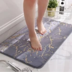 Tapete afelpado gris con diseño veteado dorado para baño, con pies descalzos y regadera.