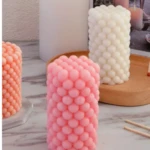 Velas cilíndricas rosas y blancas con textura de burbujas, hechas con molde de silicona, sobre mesa de mármol.