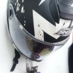 Perchero de pared plateado sostiene casco de moto negro y blanco con visor, llaves y chamarra.