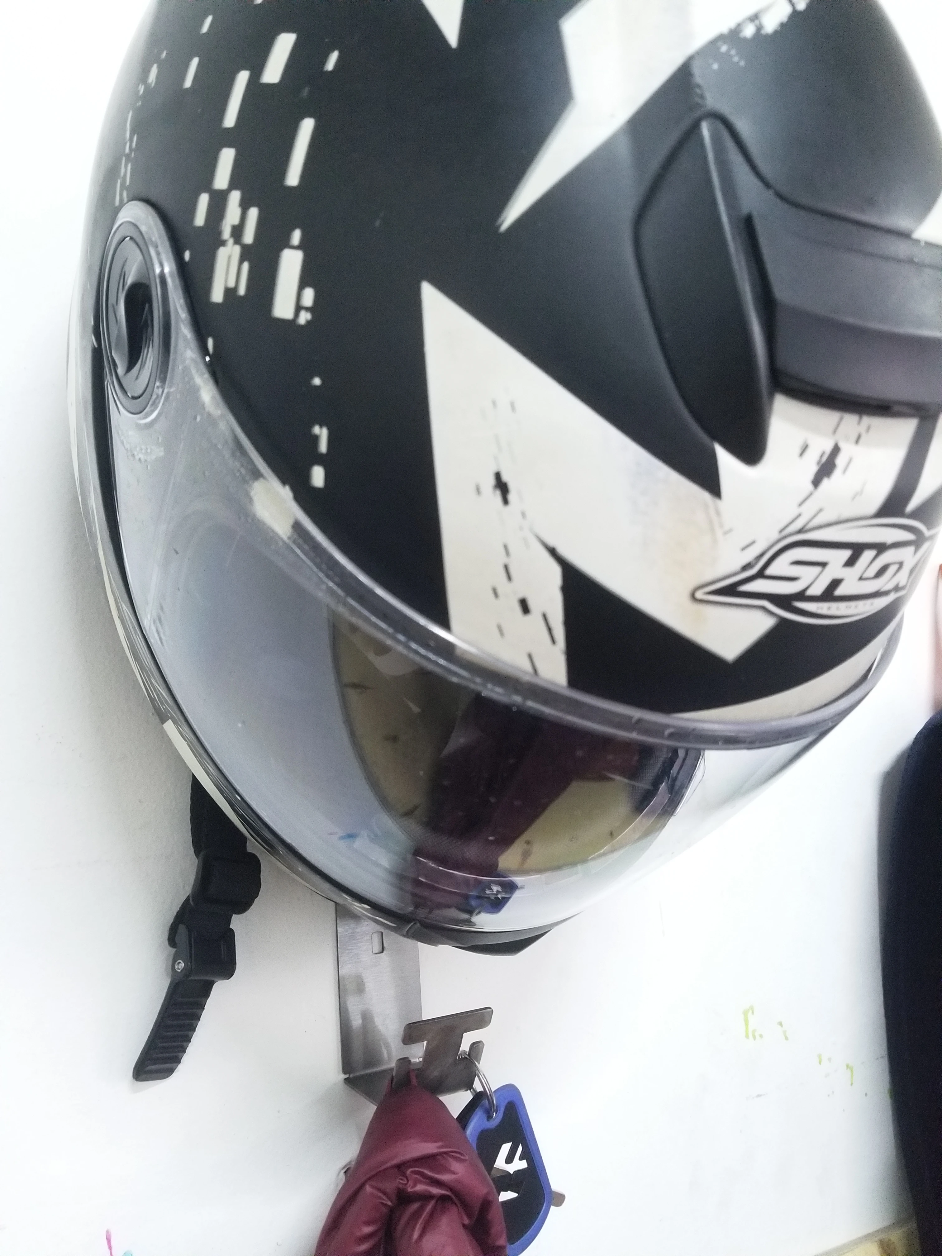 Perchero de pared plateado sostiene casco de moto negro y blanco con visor, llaves y chamarra.