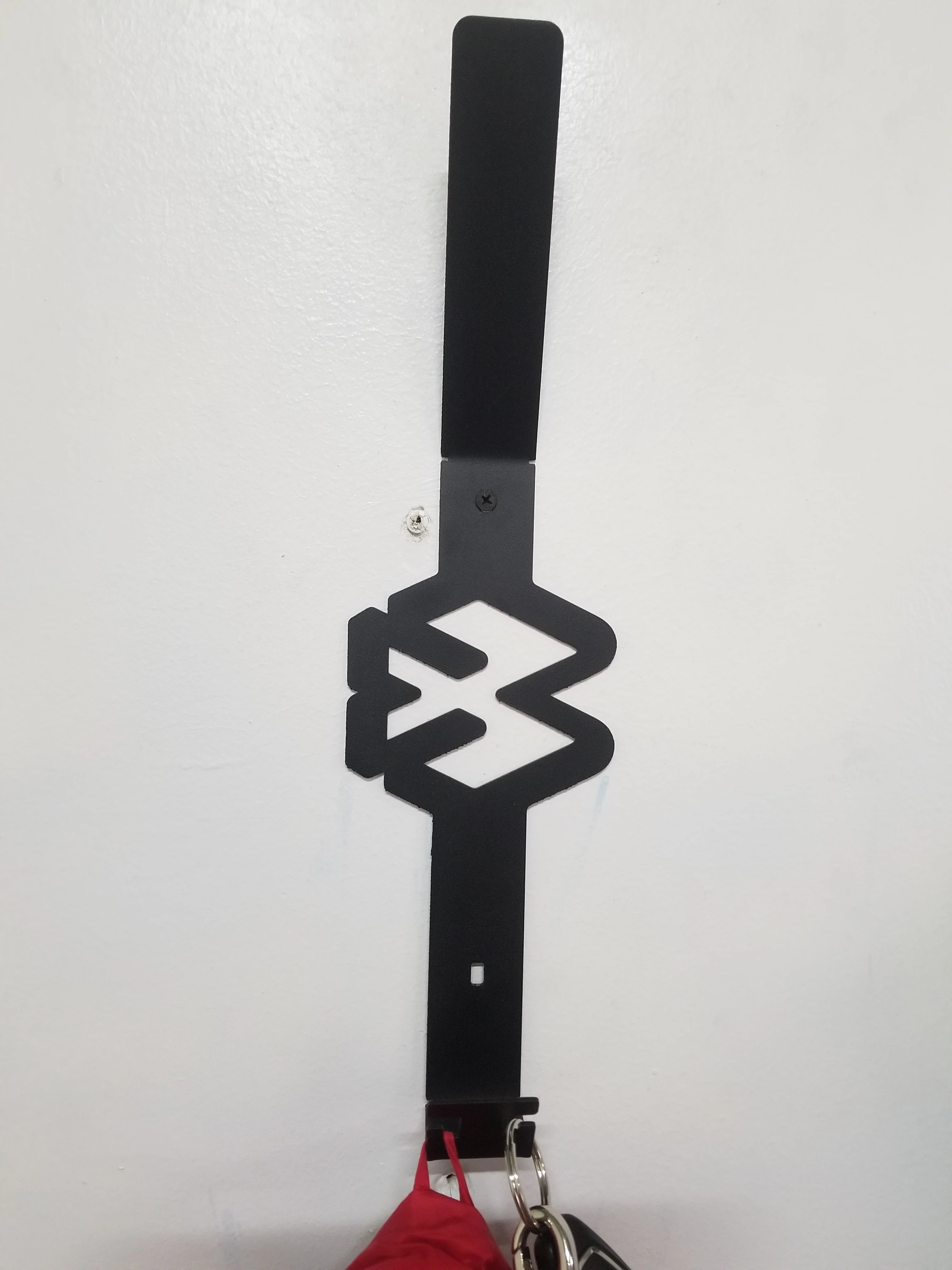Colgador de pared negro para cascos con símbolo 'W' y lugar para llaves.