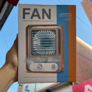 Caja de mini ventilador portátil transparente con detalles en naranja y azul, mostrando diseño y texto de producto.