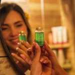 Tónico capilar anticaída en frasco de vidrio verde, con tapa dorada, con reflejo de mujer sonriente.