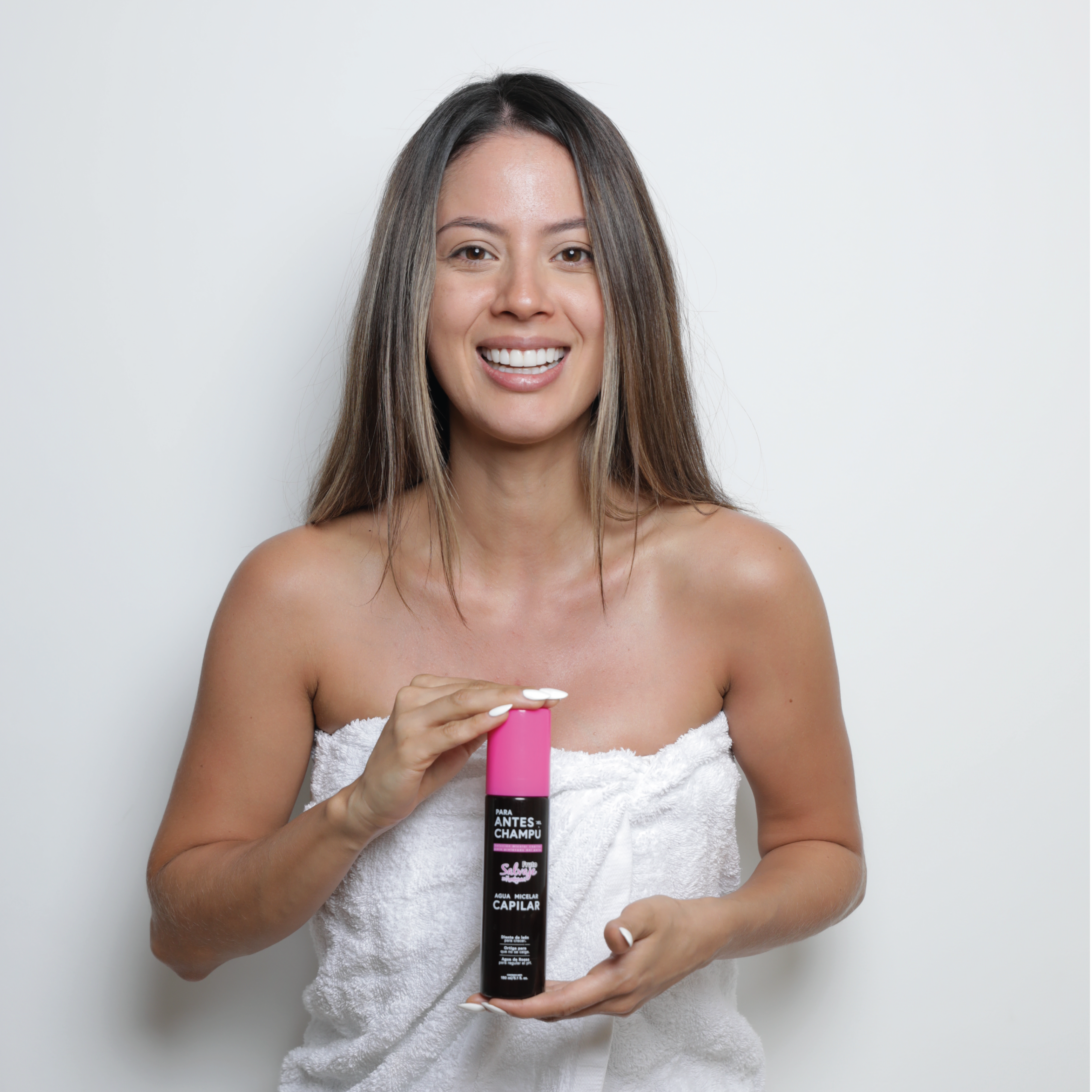 Mujer sonriente envuelta en toalla sostiene botella de agua micelar capilar Fruto Salvaje.