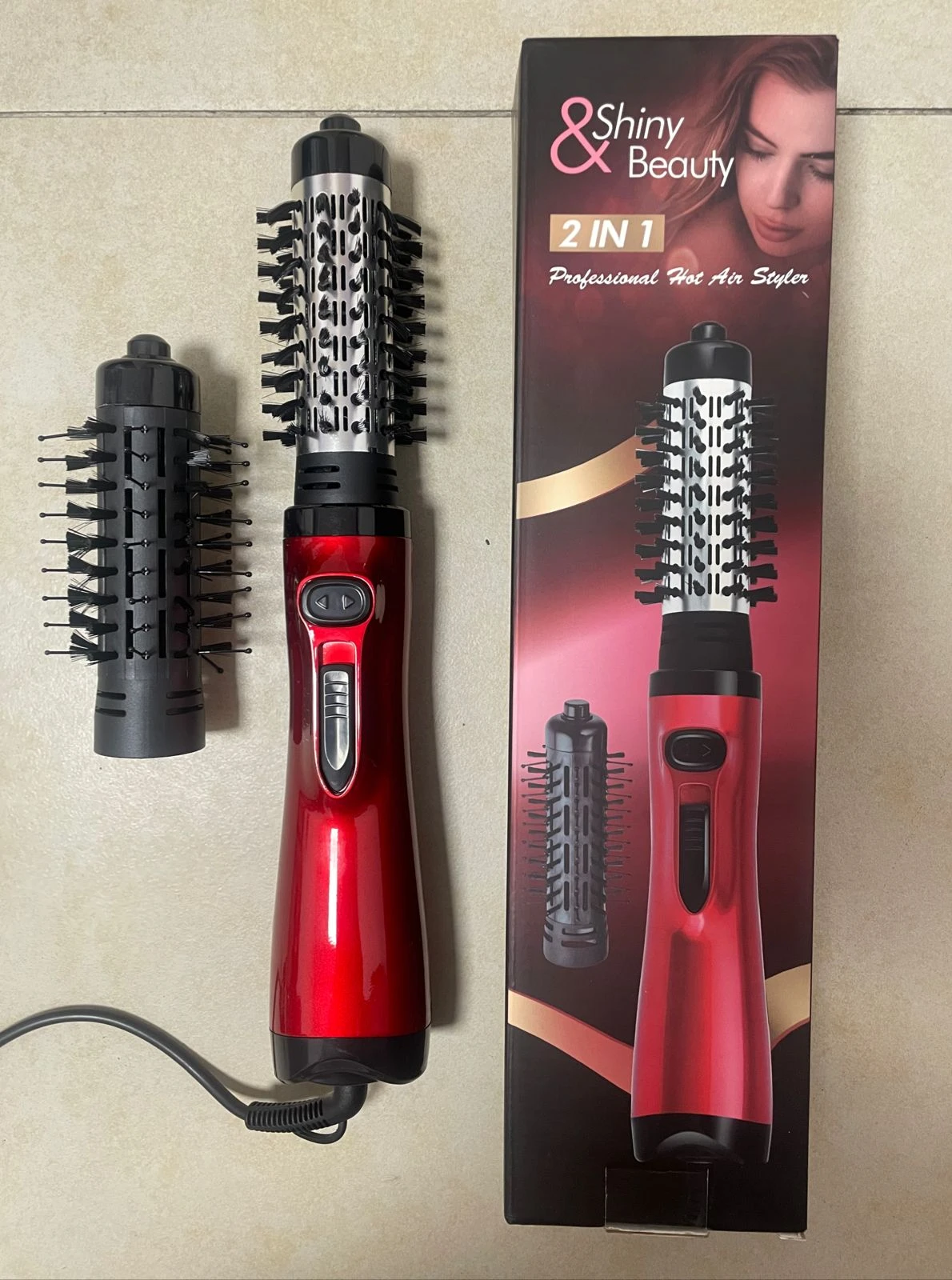 Cepillo secador alisador rojo de Shiny Beauty con mango ergonómico, un cabezal de cepillo puesto y otro intercambiable, junto a su caja original.