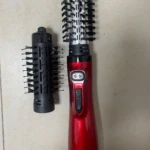 Cepillo secador alisador rojo con mango ergonómico, junto a un cabezal de repuesto desmontable con cerdas negras sobre superficie clara.