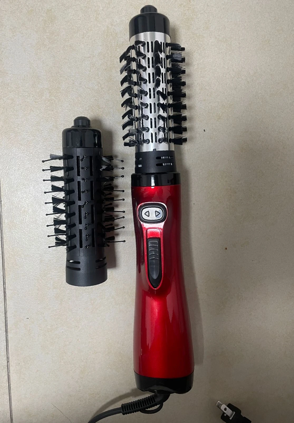 Cepillo secador alisador rojo con mango ergonómico, junto a un cabezal de repuesto desmontable con cerdas negras sobre superficie clara.