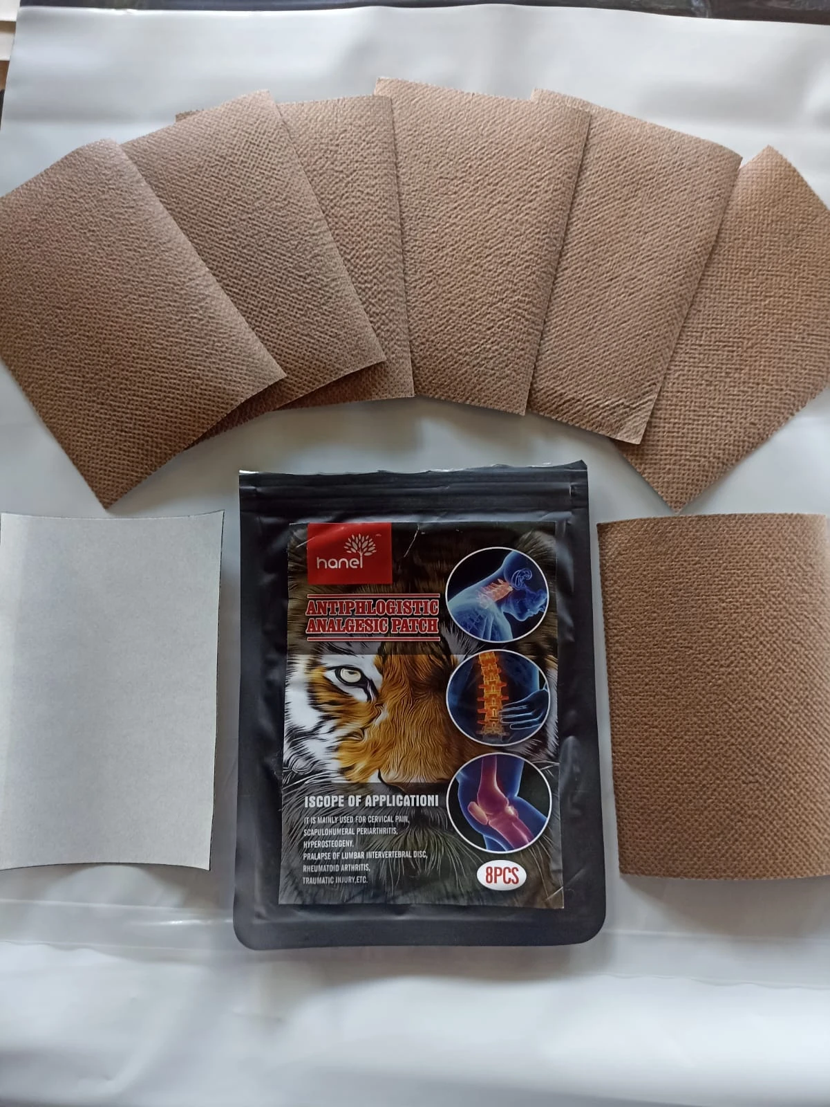 Empaque negro de 8 parches analgésicos Hanel junto a parches marrones texturizados listos para usar.