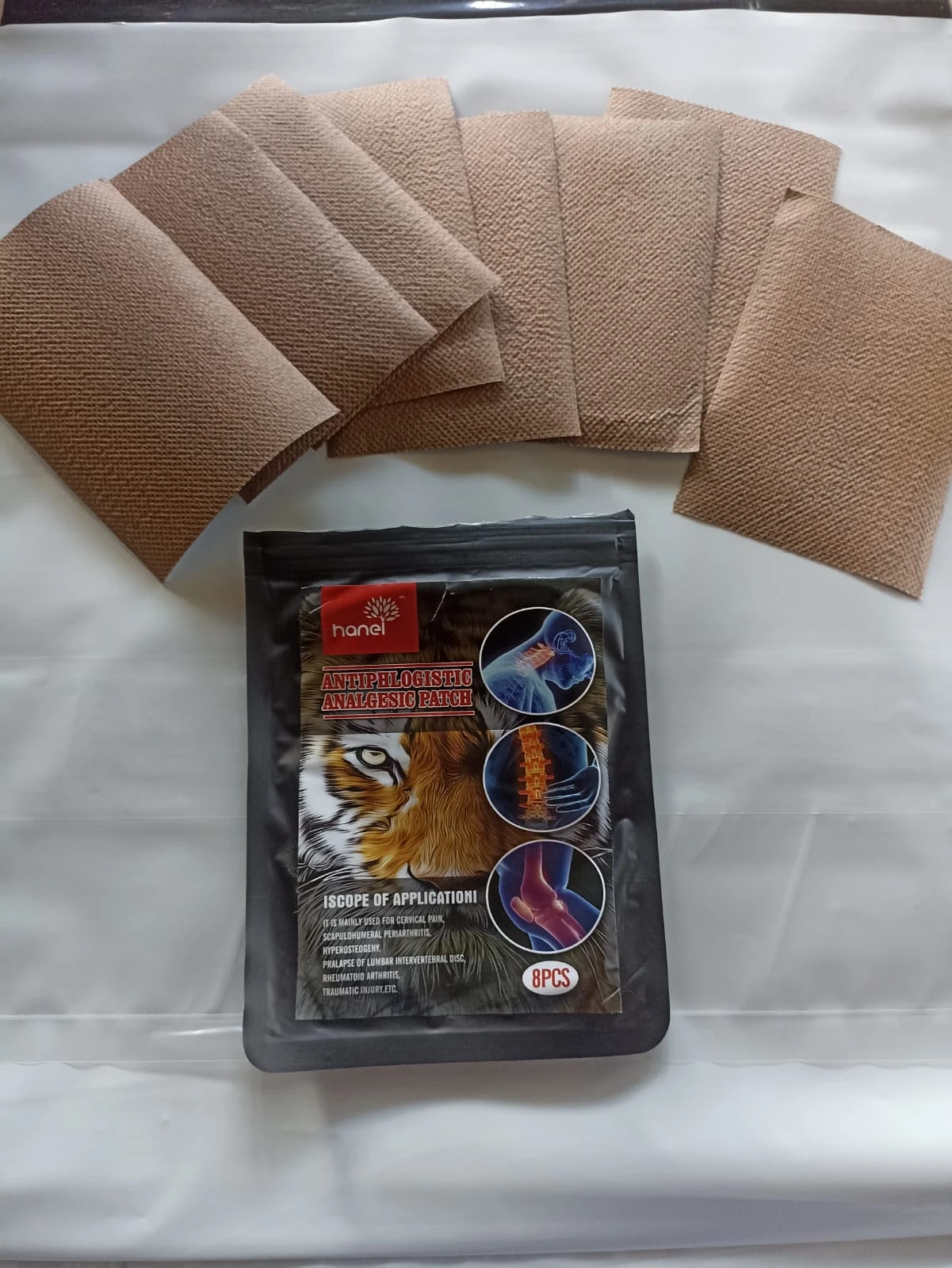 Parches analgésicos Hanel marrones texturizados con empaque negro que muestra aplicación en cuello, espalda y rodilla, 8 unidades.