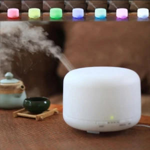 Humificador difusor aromaterapia blanco con vapor saliendo, taza té y tetera verde en mesa bambú.