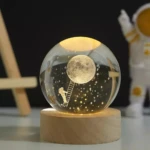Esfera de cristal con luz LED, astronauta subiendo escalera a la luna, estrellas, base de madera.
