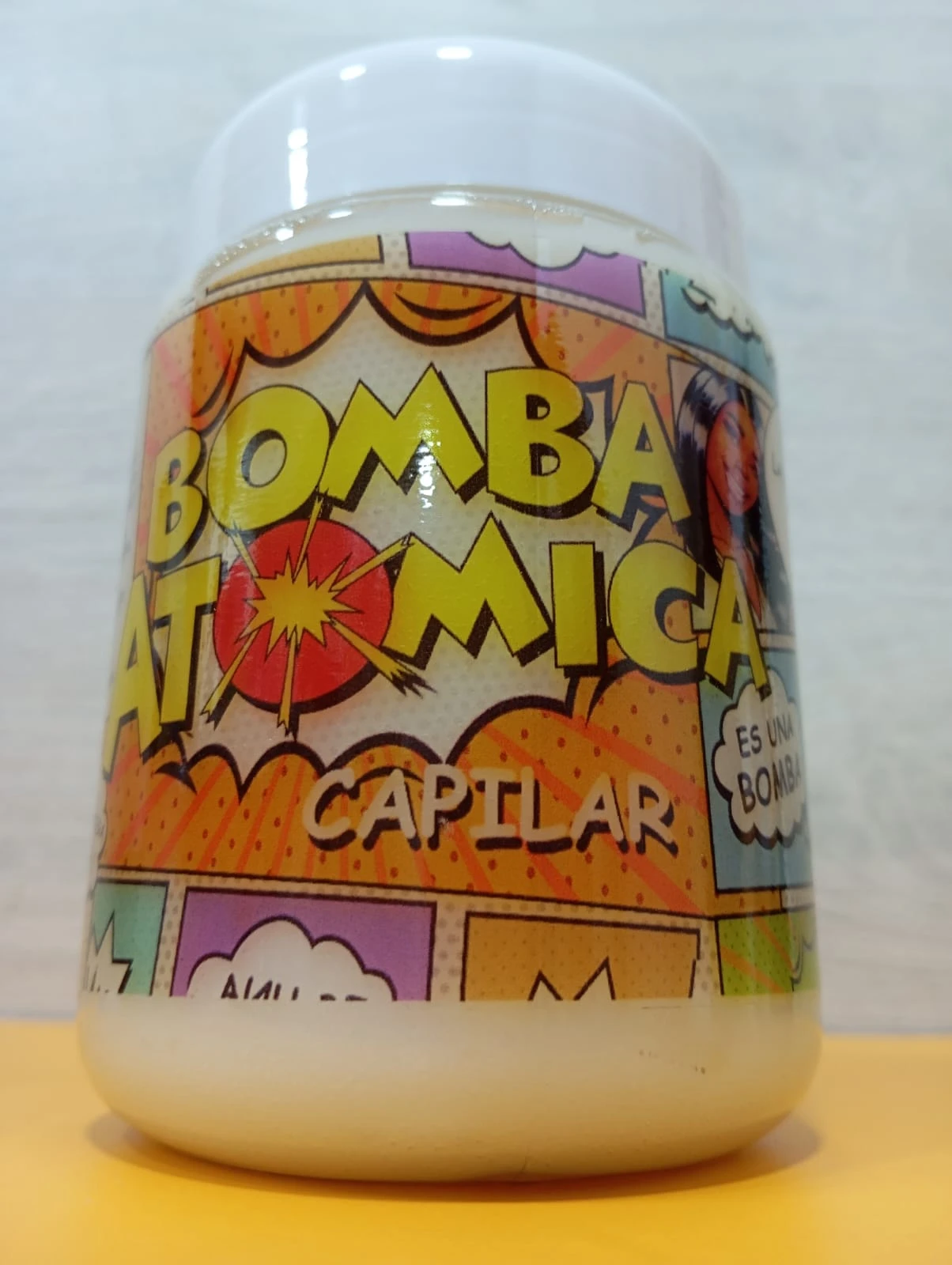 Tratamiento capilar concentrado Bomba Atómica con etiqueta cómic naranja, amarillo y detalles de explosión, aporta nutrición.