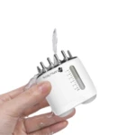 Masajeador capilar blanco con aplicador y dosificador, en mano con agua.