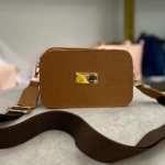 Bolso cruzado pequeño color miel con textura cocodrilo, herrajes dorados y placa "Karla Chacón". Correa ancha oscura.