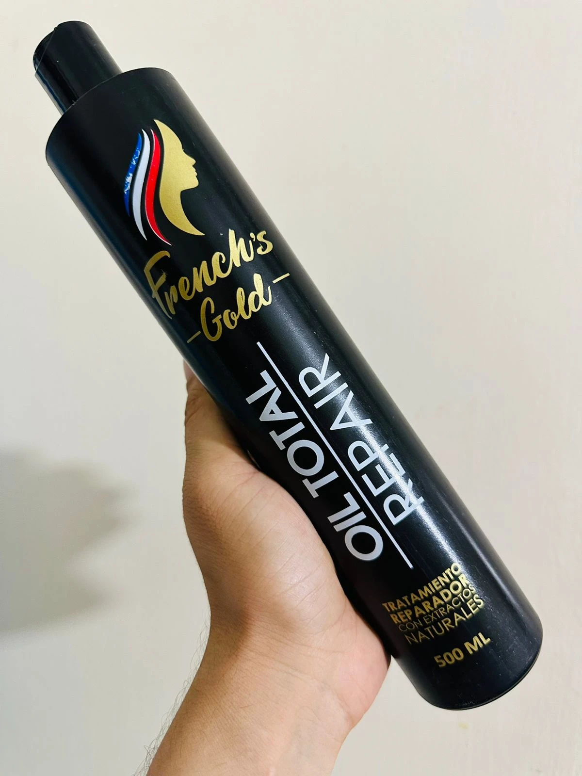 Botella negra de repolarizador capilar French's Gold Oil Total Repair 500ml, en mano.