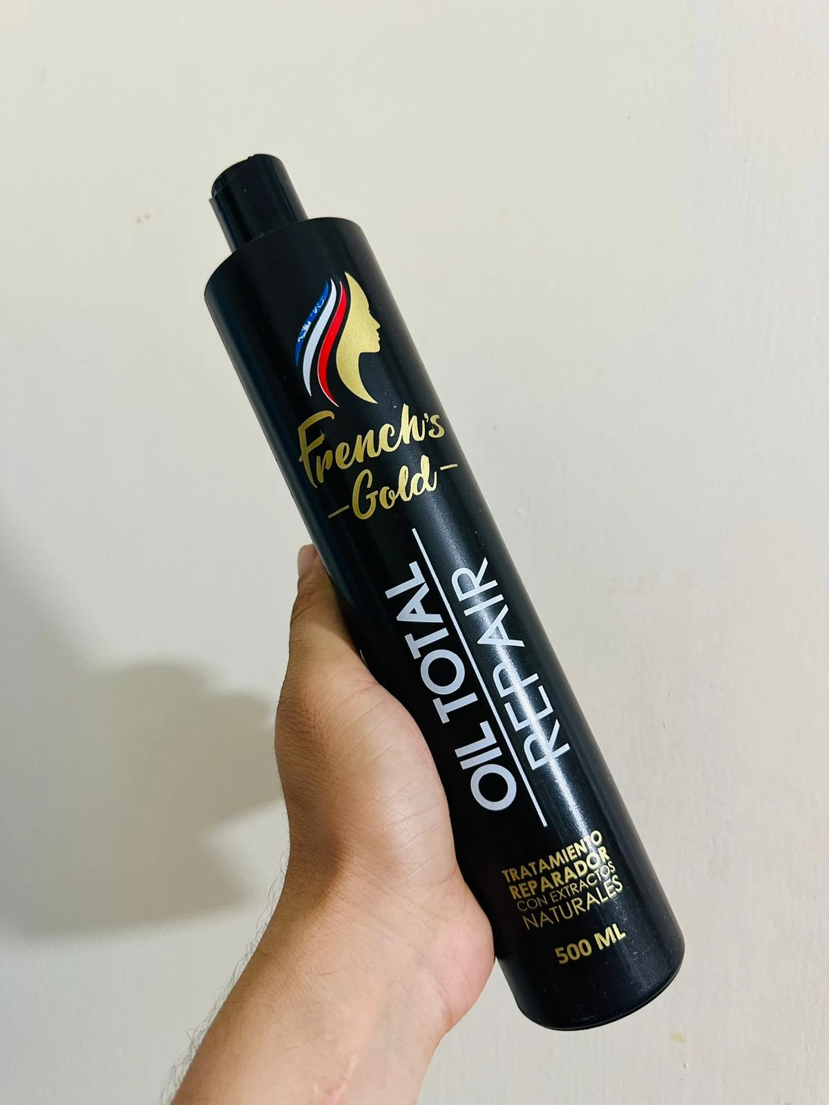 Botella negra de French's Gold Oil Total Repair 500ml con logo de mujer y escudo, sostenida en mano.