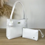 Bolso tote blanco sintético Karla Chacon Gema, asa doble, con llavero pompón blanco y neceser a juego sobre mesa de madera.