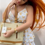 Mujer pelirroja luce bolso tote beige y café con etiqueta Karla Chacón, estampado floral y reloj dorado.