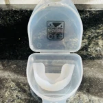 Protector bucal blanco translúcido Sport Life dentro de su estuche abierto sobre superficie de granito oscuro.