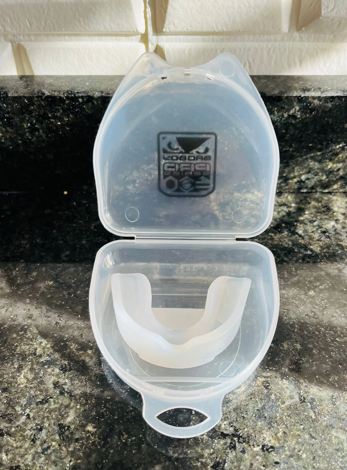 Protector bucal blanco translúcido Sport Life dentro de su estuche abierto sobre superficie de granito oscuro.