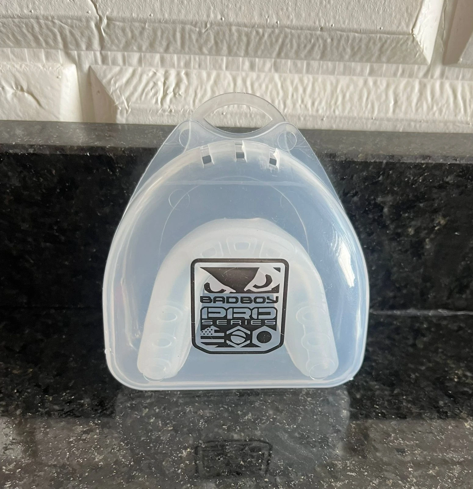 Protector bucal blanco "Bad Boy Pro Series" en estuche plástico translúcido sobre superficie oscura veteada.