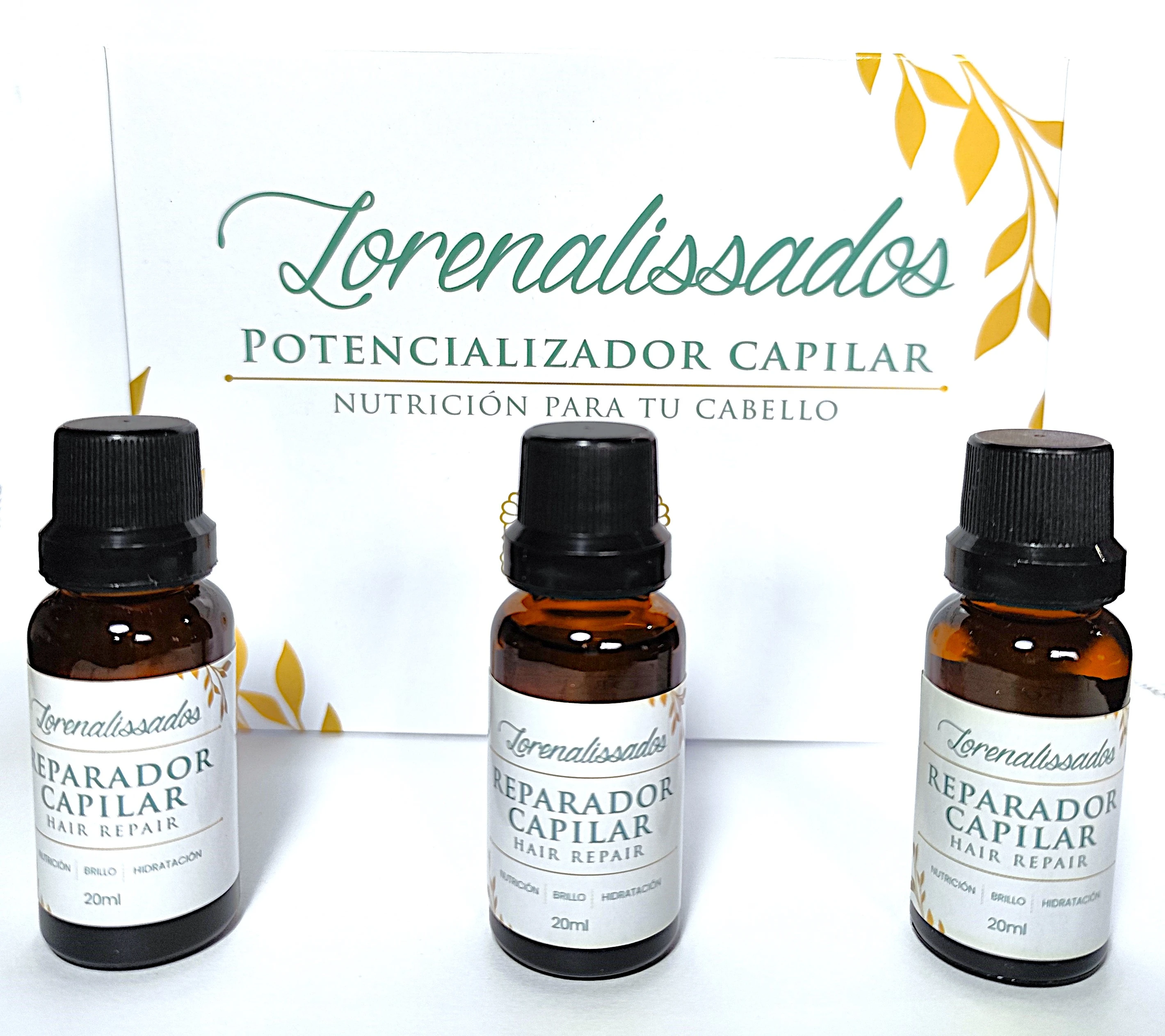 Tres frascos de vidrio ámbar con gotas aplicador y tapa negra, etiquetas blancas con letras verdes: "Reparador Capilar Hair Repair" y detalles botánicos dorados.