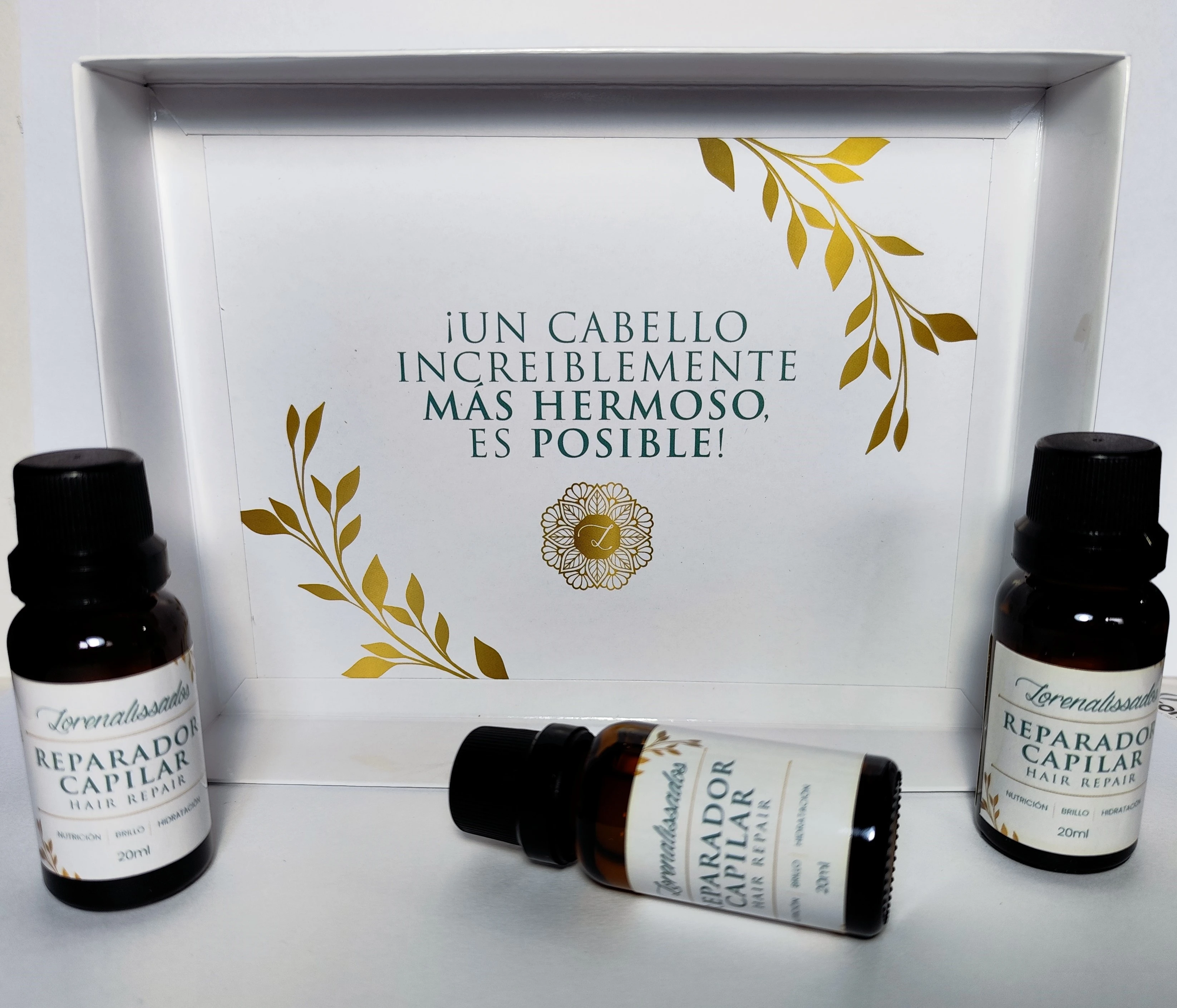 Tres frascos ámbar con tratamiento capilar reparador, caja blanca con diseño floral dorado, texto "¡Un cabello increíblemente más hermoso, es posible!".