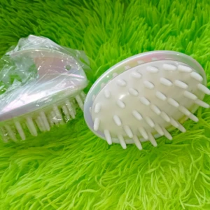 Cepillo masajeador capilar tornasol con cerdas blancas, uno cubierto en plástico, sobre fondo verde peludo.