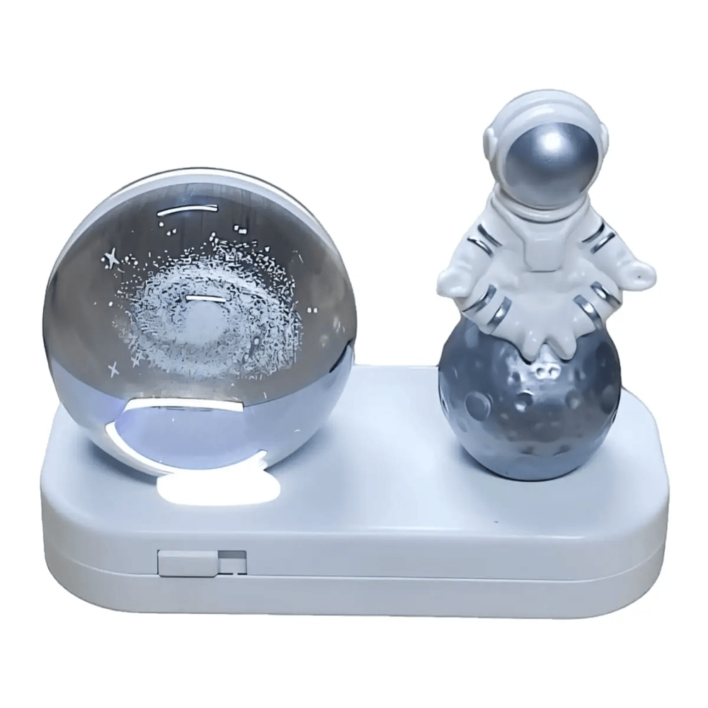 Esfera iluminada de galaxia con astronauta sentado en la luna, base blanca con interruptor.