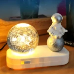 Esfera de cristal con galaxia iluminada y astronauta en luna, base LED blanca.