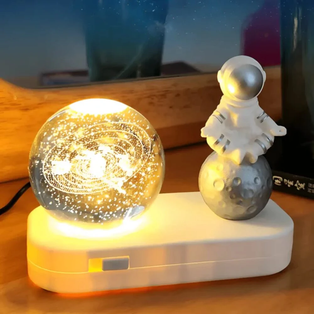Esfera de cristal con galaxia iluminada y astronauta en luna, base LED blanca.