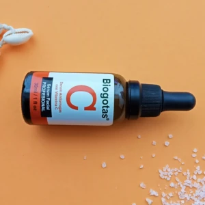Serum facial Biogotas con Vitamina C, presentación 30ml, con conchas y sal sobre fondo naranja.