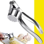 Triturador de ajos plateado en acción, con ajos enteros y picados al lado.