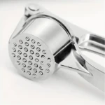 Triturador machacador de ajos metálico plateado con orificios, ideal para cocina.