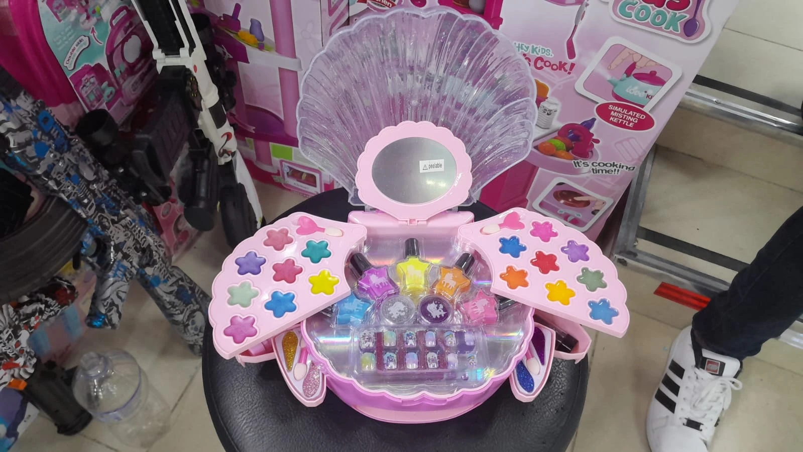 Set de maquillaje infantil en estuche rosa con forma de concha abierta, incluye sombras en forma de estrella, esmaltes, brillos y aplicadores.