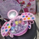 Set de maquillaje infantil con estuche rosa en forma de concha desplegable que incluye variedad de sombras, labiales, esmaltes y aplicadores.