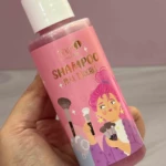 Botella rosa de shampoo para brochas de maquillaje con caricaturesca y tapa blanca.