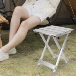 Mesa plegable metálica plateada en uso exterior, junto a persona sentada.