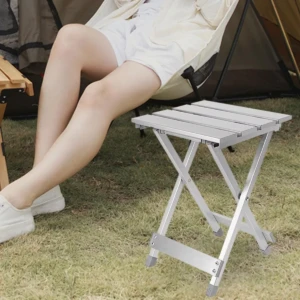 Mesa plegable metálica plateada en uso exterior, junto a persona sentada.