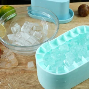 Molde de silicona celeste para cubos de hielo con cubos llenos y otros esparcidos en cuenco de cristal.