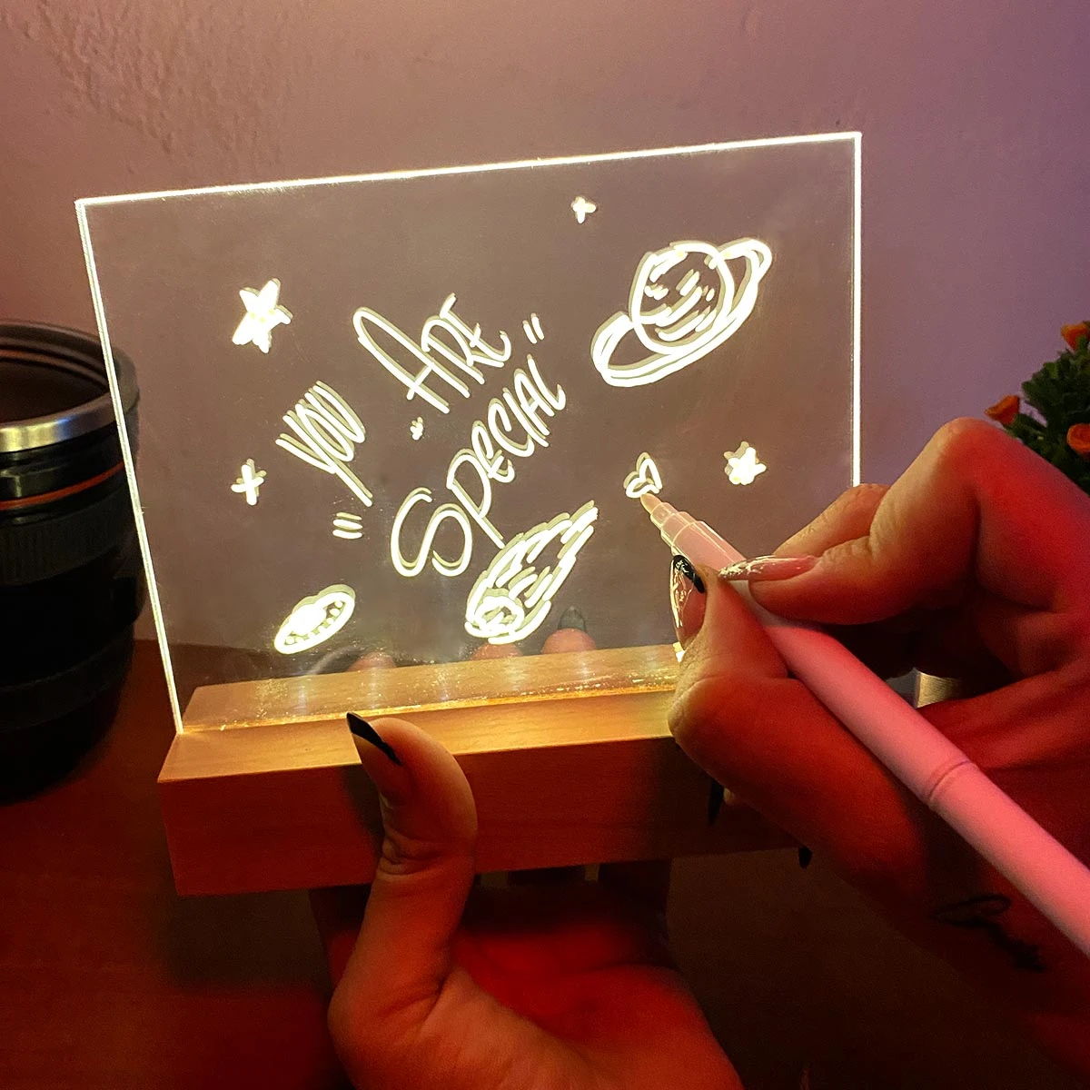 Lámpara LED acrílica borrable con mensaje "You are special", fondo espacial, base de madera, y mano escribiendo.