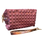 Cartuchera/cosmetiquera rosa metalizada con tachas piramidales y correa de mano dorada.