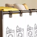 Cesta organizadora de ropa X1 con cortinas blancas decoradas con lavadoras, sobre rieles oscuros y cojines de fondo.